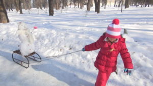 ребенок катает снеговика на санках